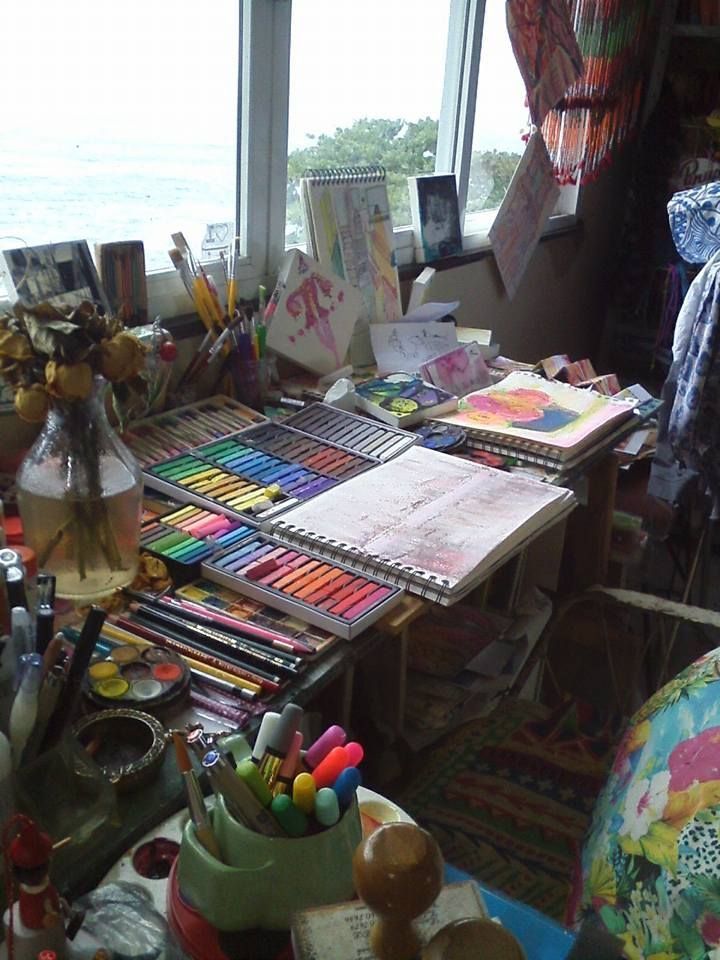 a messy desk with lots of art supplies on it and a large window in the background