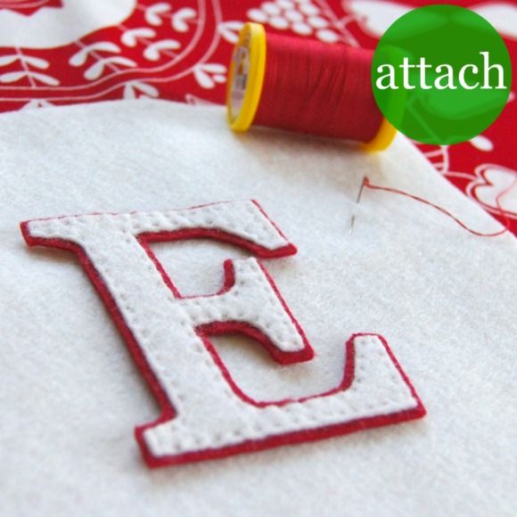 the letter e is made out of white fabric with red thread next to it and a spool of thread