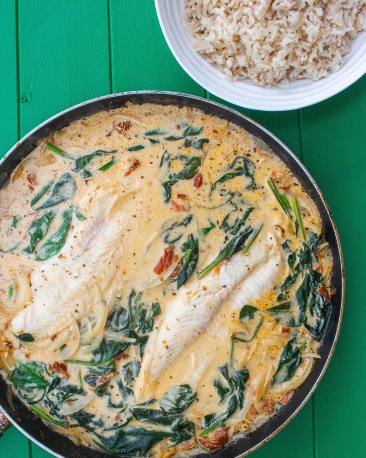 a pan filled with chicken and spinach covered in sauce next to rice on a green table