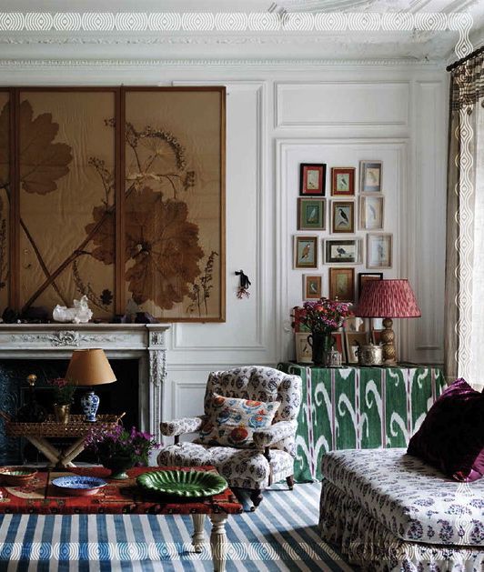 a living room filled with lots of furniture and paintings on the wall above it's fireplace