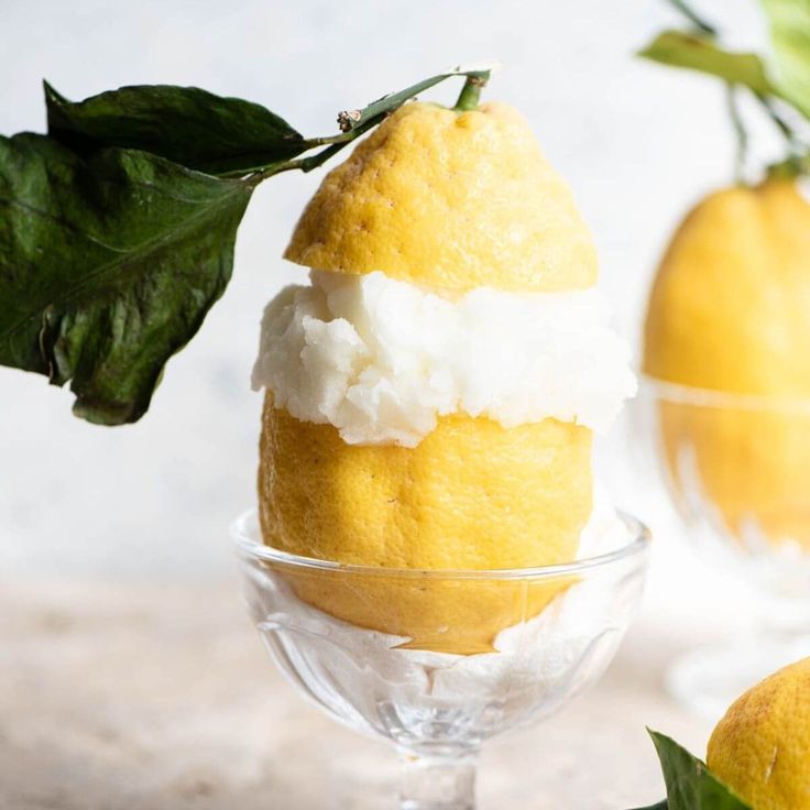 two lemons with ice cream and leaves in small glass bowls on a counter top