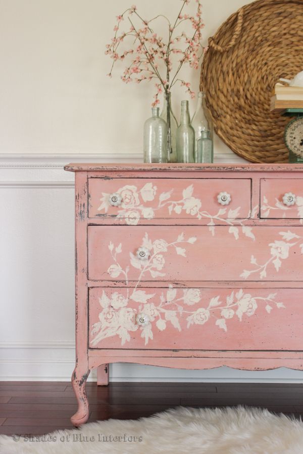 a pink dresser with flowers painted on it and a clock in the corner next to it