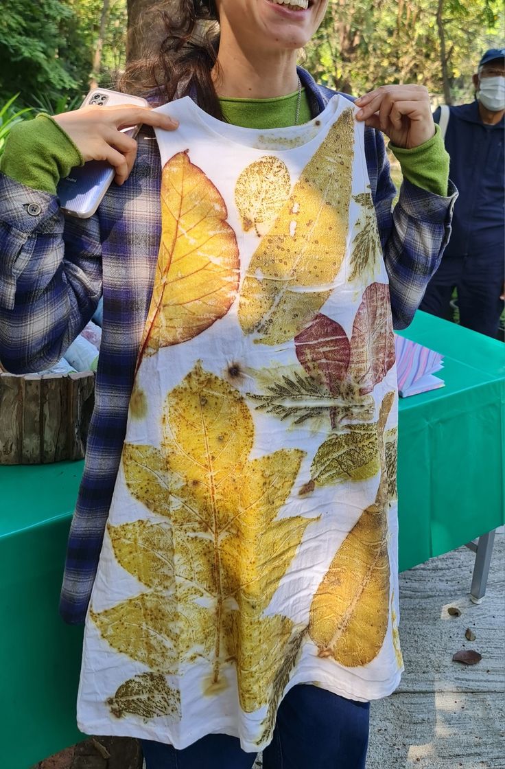 a woman standing next to a tree wearing a shirt with leaves on it and smiling at the camera