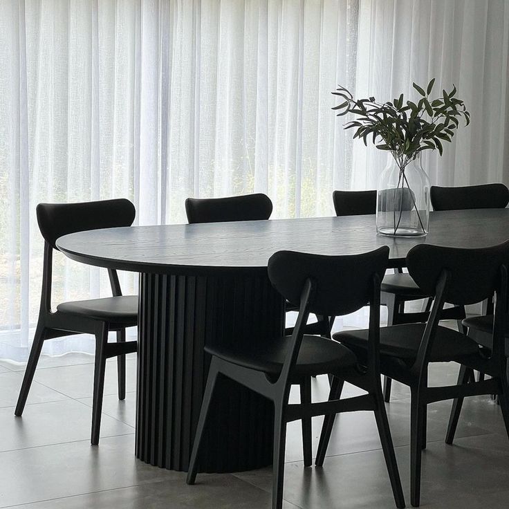 a dining room table with black chairs and a vase on the table next to it