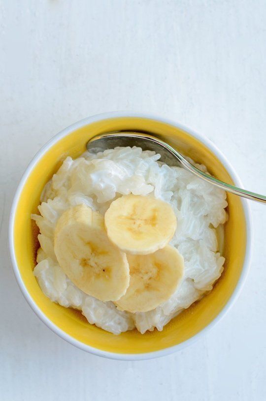 a bowl filled with rice and sliced bananas on top of a white tablecloth next to a spoon