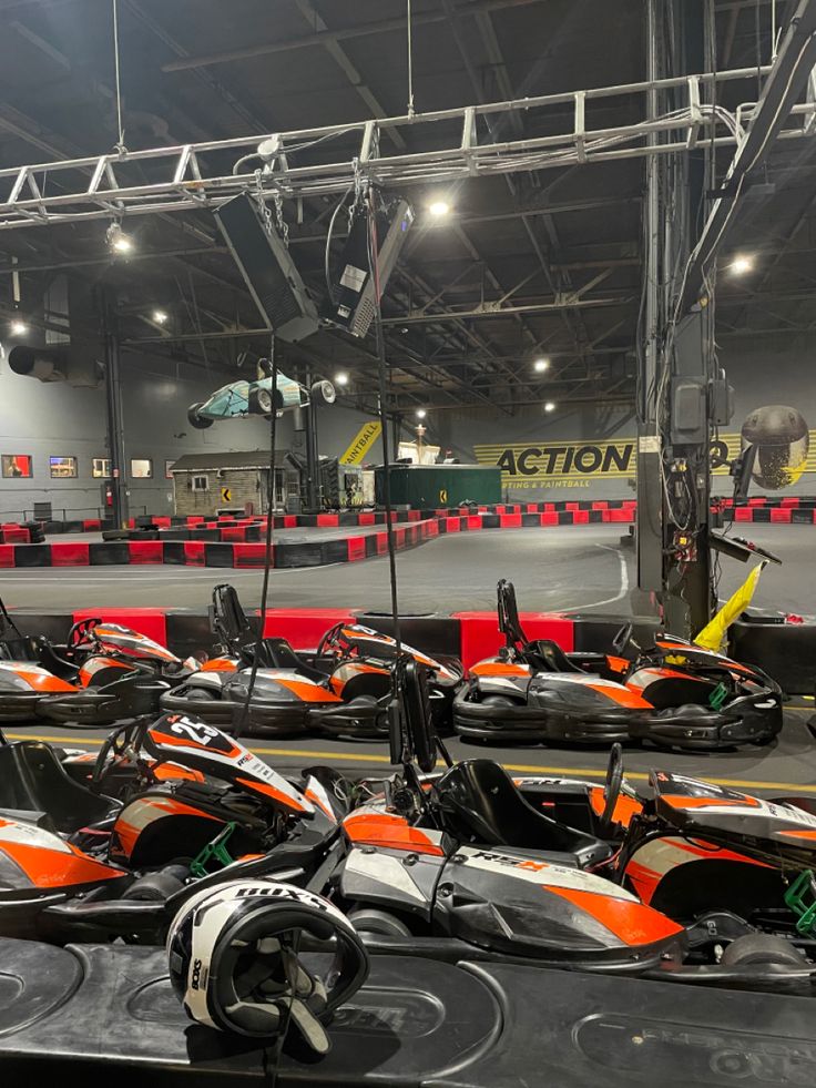 several orange and black go karts lined up in an indoor race track with lights on