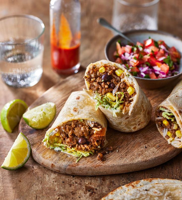 two burritos cut in half on a cutting board next to a bowl of salsa