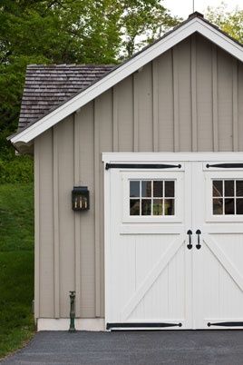 a garage with two doors and windows on the side of it in front of some trees