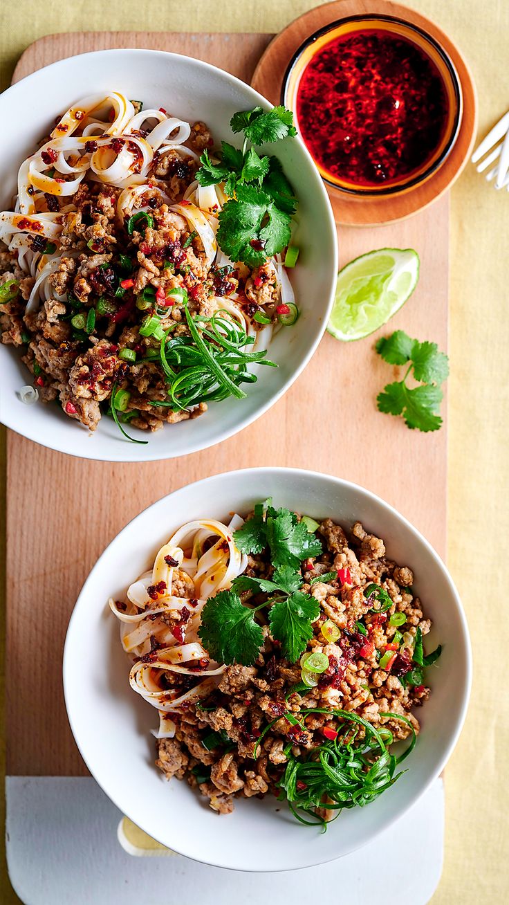 two white bowls filled with food on top of a wooden cutting board