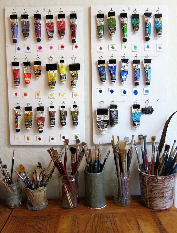 there are many paint brushes in buckets next to each other on the table with cups