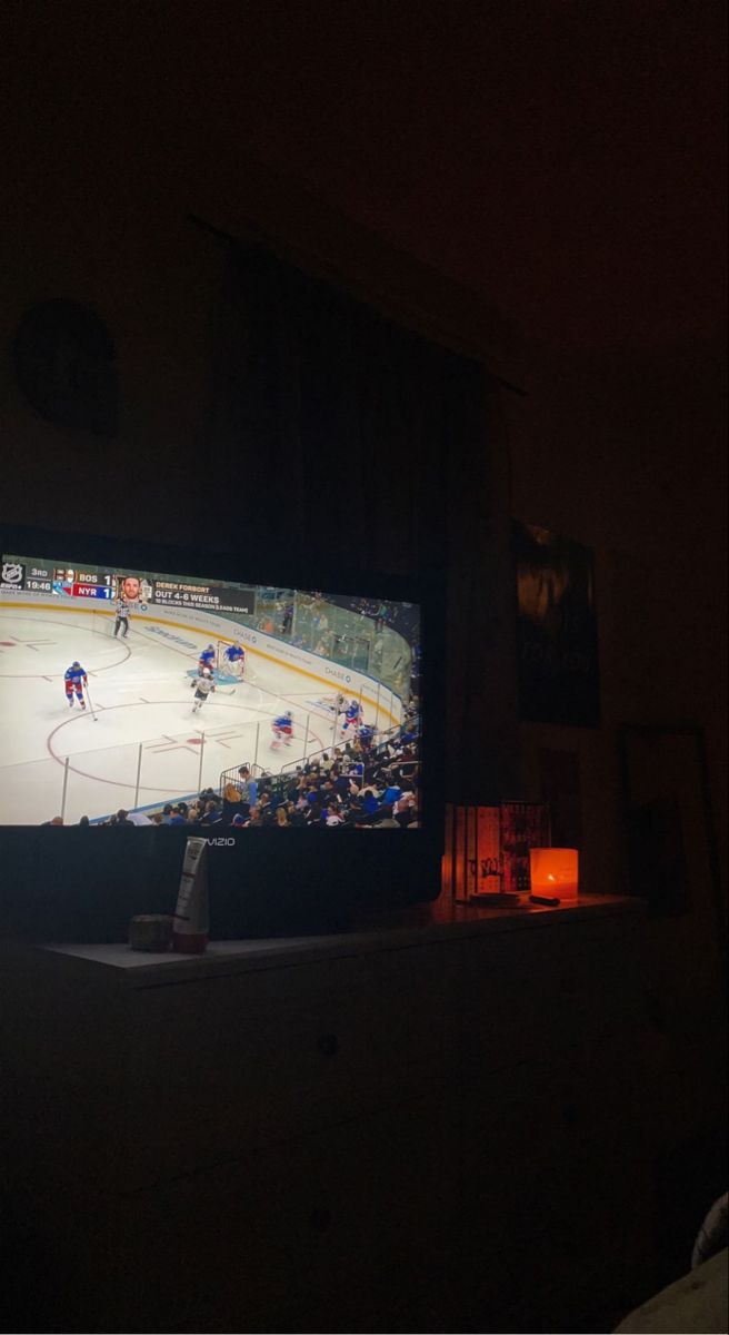 a hockey game is shown on the tv screen in this dark room with an orange light