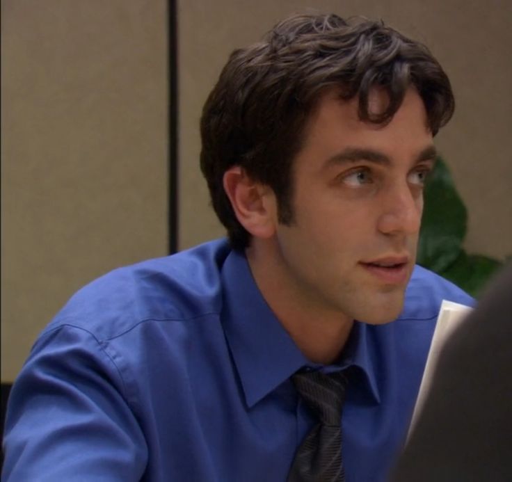 a man in a blue shirt and tie sitting at a desk looking off to the side