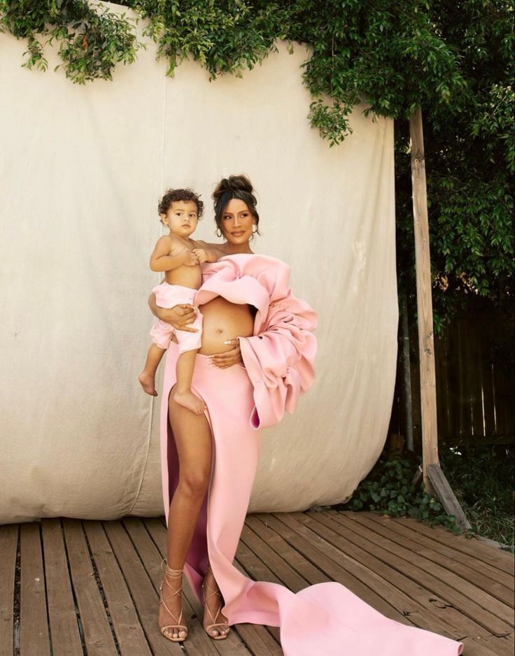 a woman holding a baby in her arms and standing on a wooden floor next to a wall