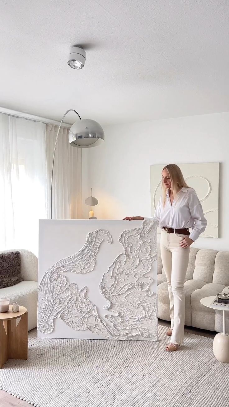 a woman standing next to a large sculpture in a living room with white walls and furniture