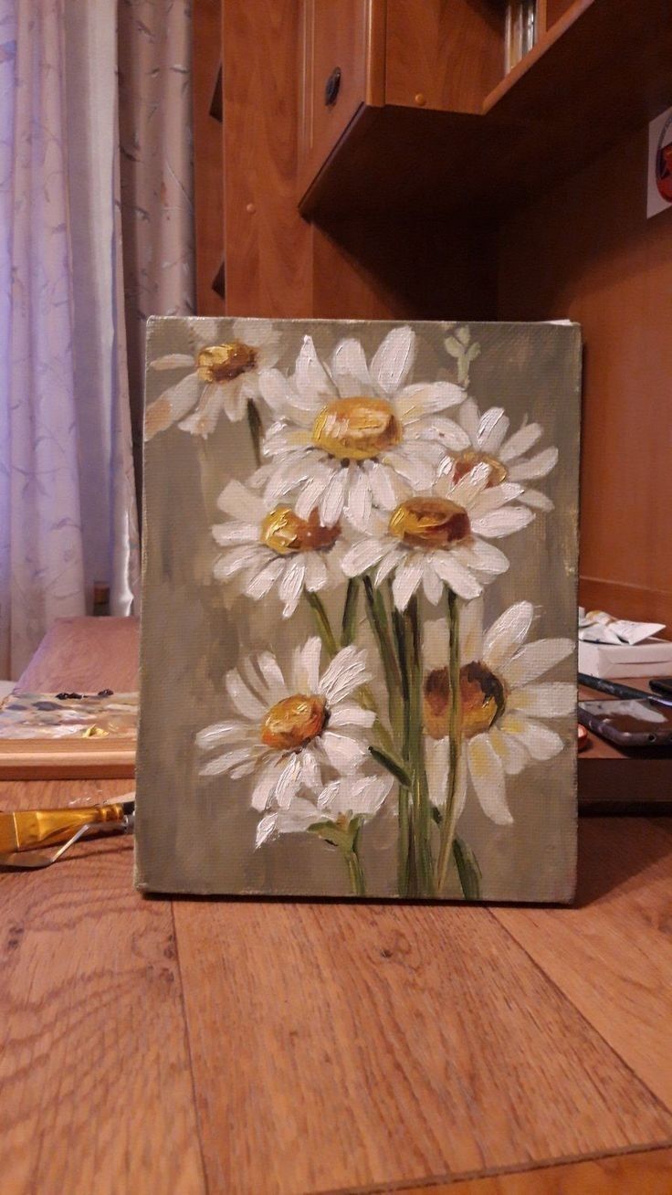 a painting of white daisies on a wood floor in front of a kitchen cabinet