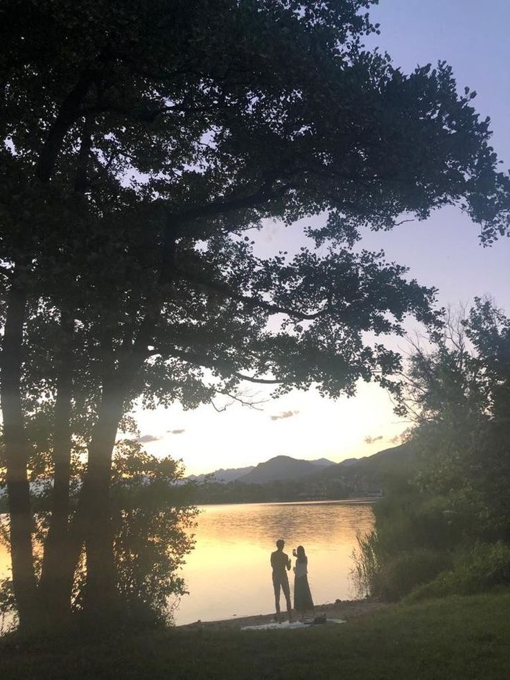 two people are standing by the water at sunset