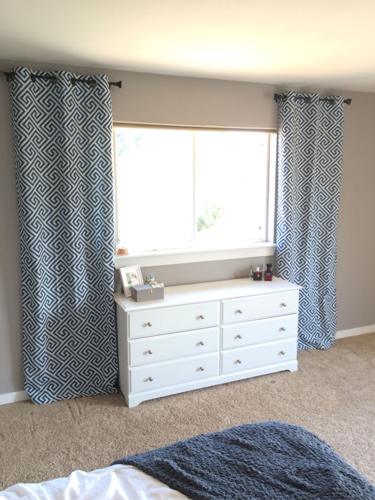 a bedroom with a bed, dresser and window in the corner that has blue curtains on it