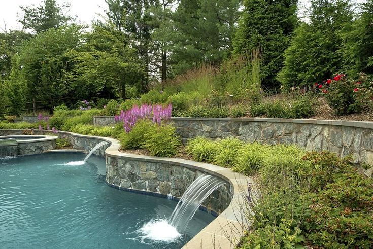 an outdoor swimming pool surrounded by stone walls and water features, with a waterfall running down the side