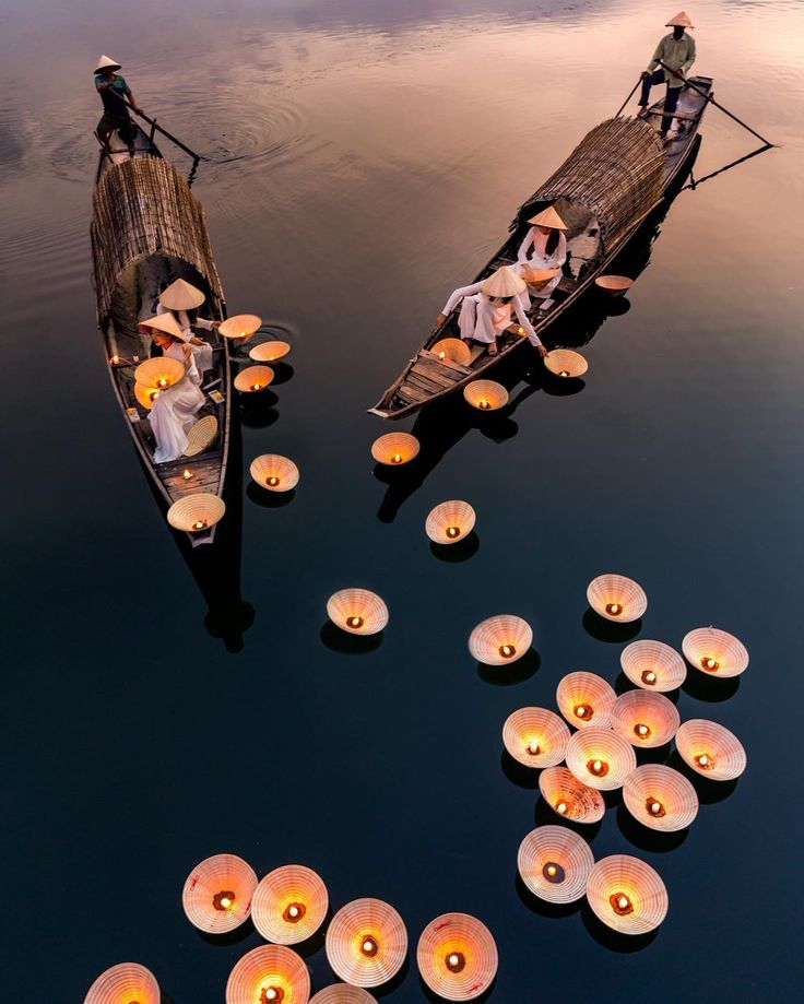 two boats with candles floating on water next to each other and people in the boat