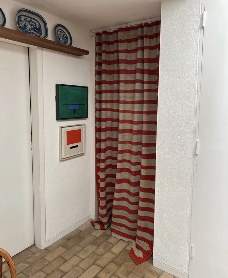 there is a red and white striped curtain in the corner of this room with two plates on the wall