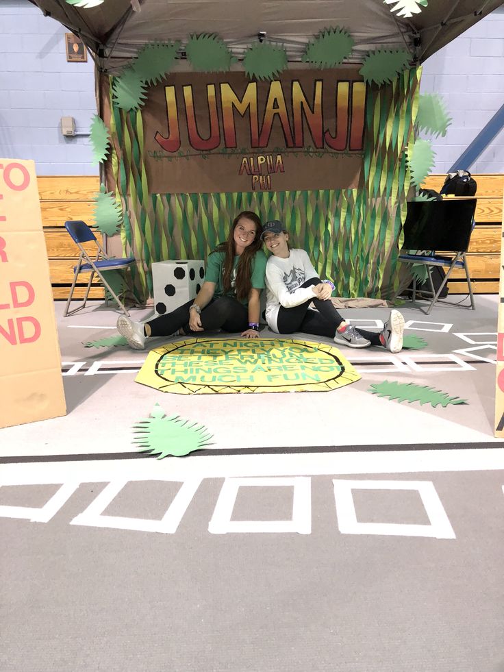 two people sitting on the ground in front of a sign that says jumanu