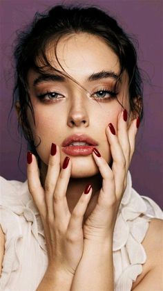 a woman with red nail polish holding her hands to her face and looking at the camera