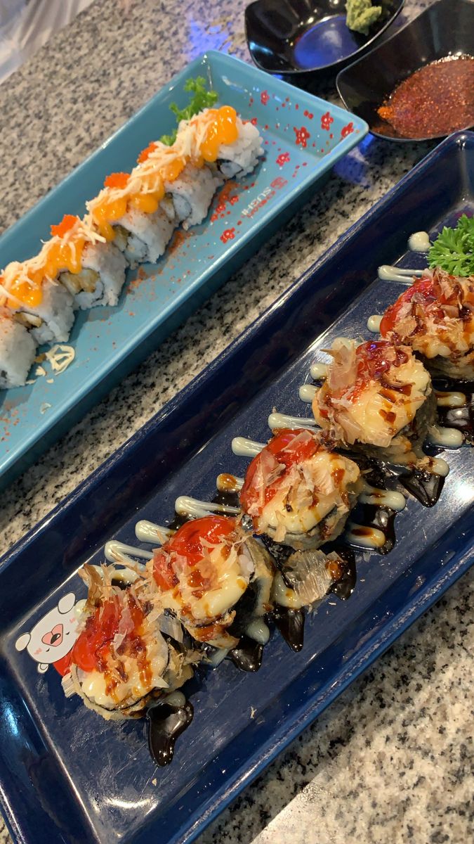 sushi and other food items on blue serving trays sitting on granite counter top