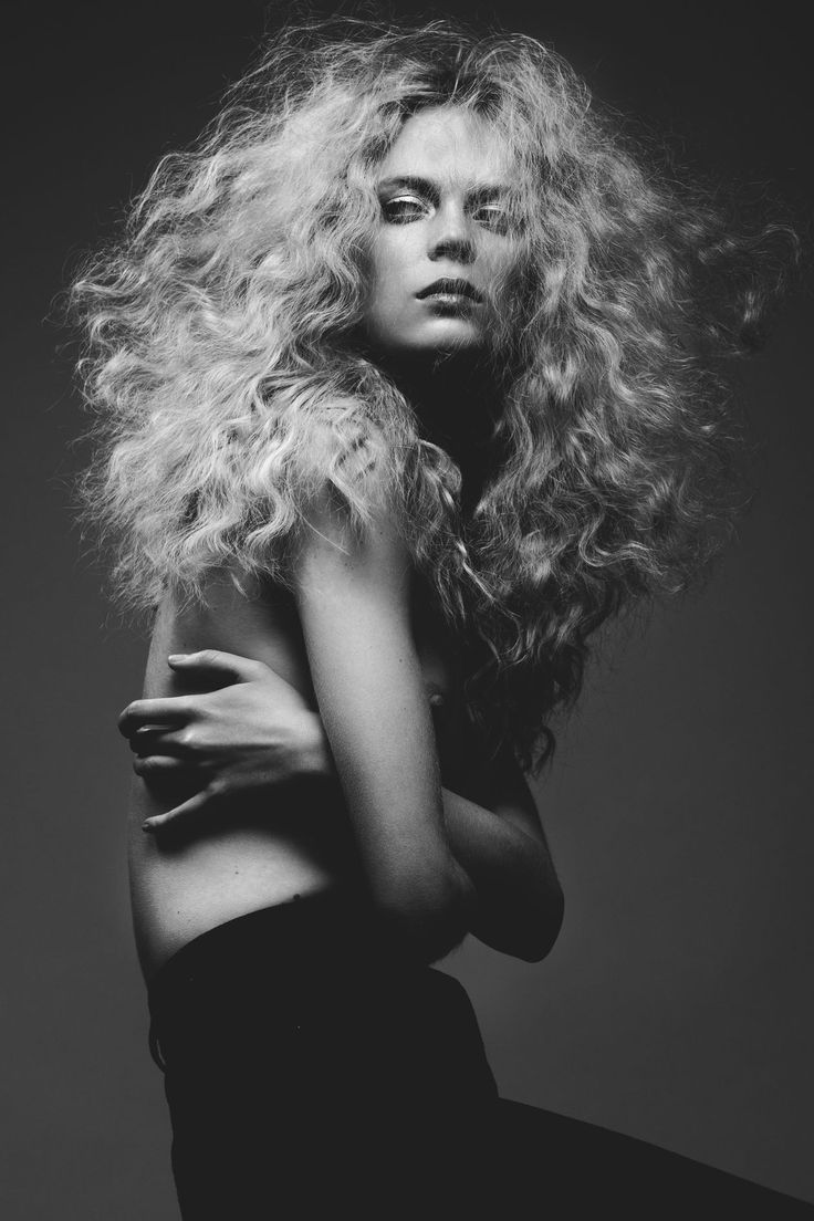 a black and white photo of a woman with long curly hair, wearing a dress