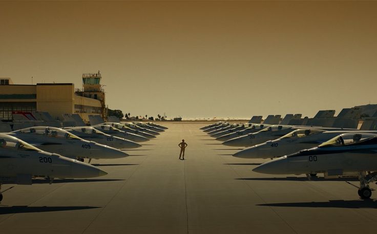 a man standing in front of rows of parked airplanes on an airport tarmac at sunset