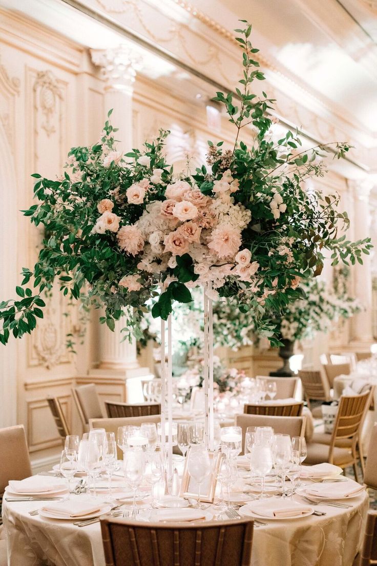 a tall vase filled with flowers and greenery on top of a white table cloth