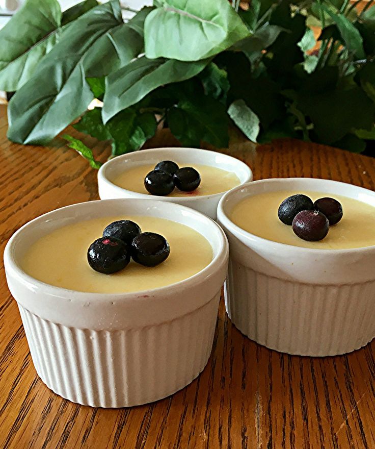 three small white bowls filled with food on top of a wooden table next to a plant