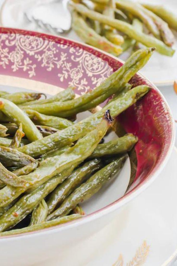 green beans in a red and white bowl on a plate next to silver spoons