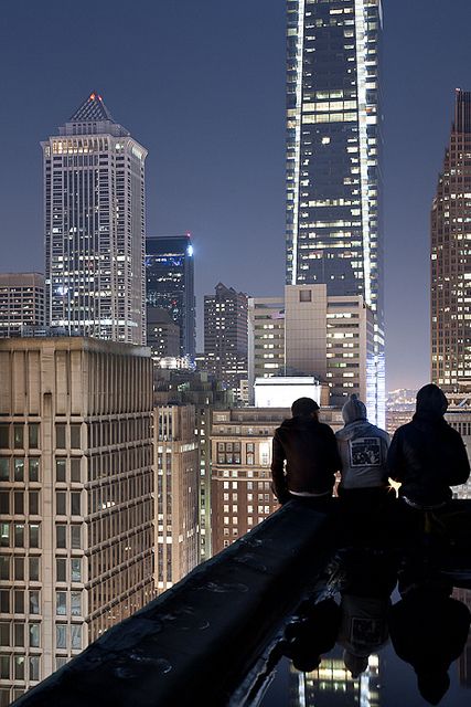 three people sitting on top of a roof looking at the city skyline in black and white