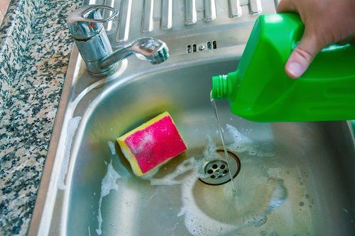 a person is washing their hands in a sink with soap and water from a green bottle