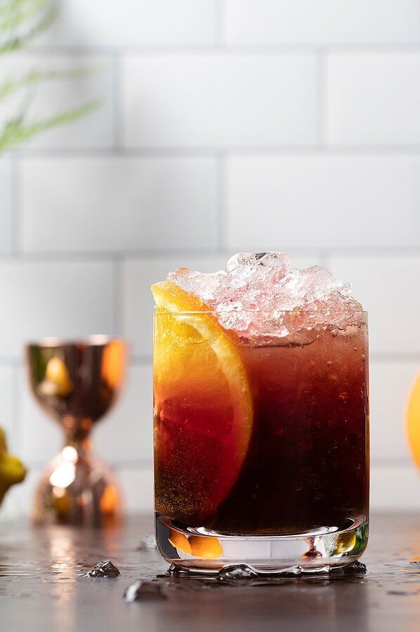 a close up of a drink in a glass on a table with lemons around it