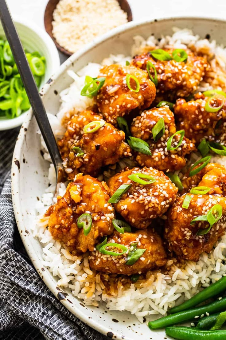 a white plate topped with rice and meat covered in sesame seeds next to green beans