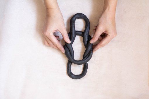 two hands holding a large black chain on top of a white sheet in the shape of a heart