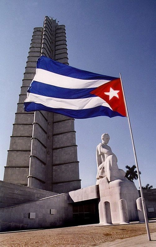 a large flag flying in front of a tall building with a statue on it's side