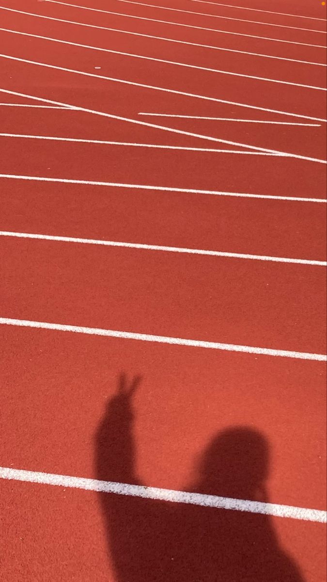 the shadow of a person on a running track with their hand up in the air