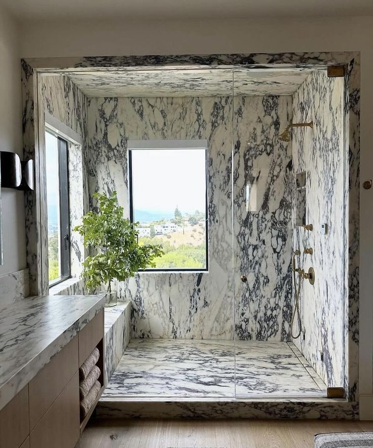 a bathroom with marbled walls and flooring next to a large window that looks out onto the countryside