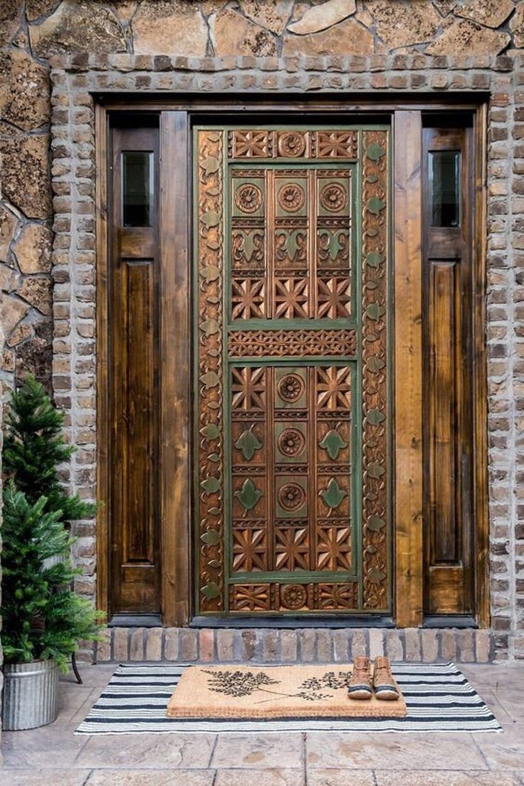 an ornate wooden door in front of a stone building with potted plants on the side