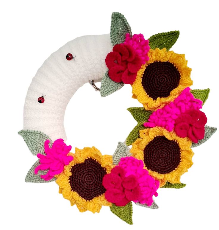 a knitted wreath with sunflowers and leaves on it, sitting in front of a white background