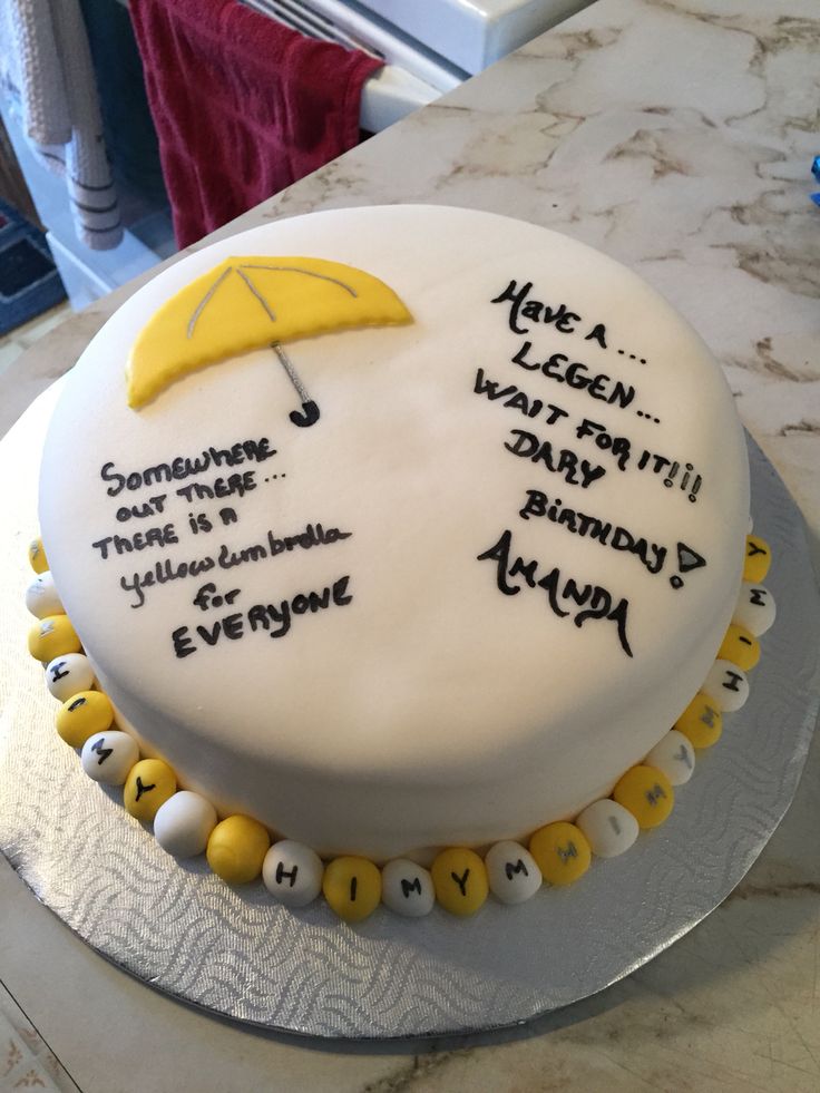 a white cake with yellow and black writing on it that has an umbrella over the top