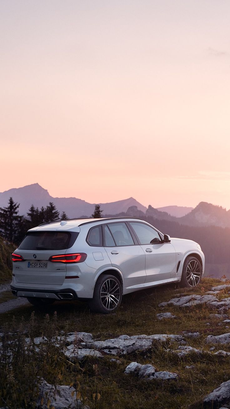 a white bmw suv parked on top of a hill