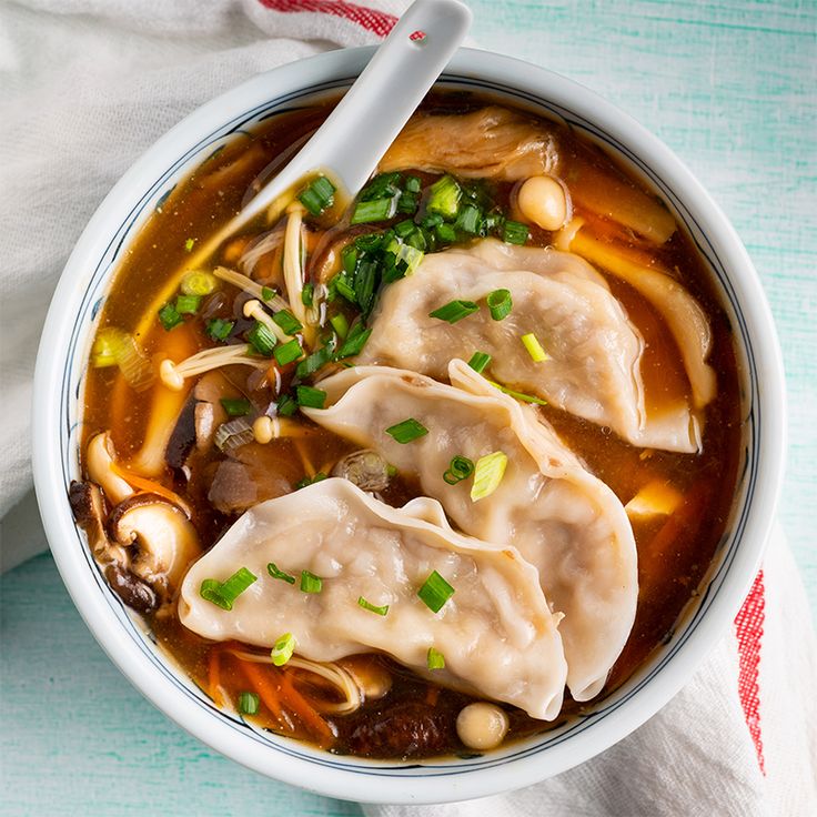 a bowl filled with dumplings and vegetables on top of a white cloth next to a spoon