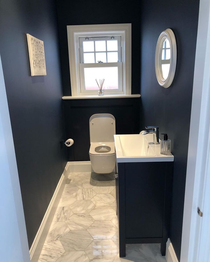 a white toilet sitting next to a sink in a bathroom under a window with a round mirror