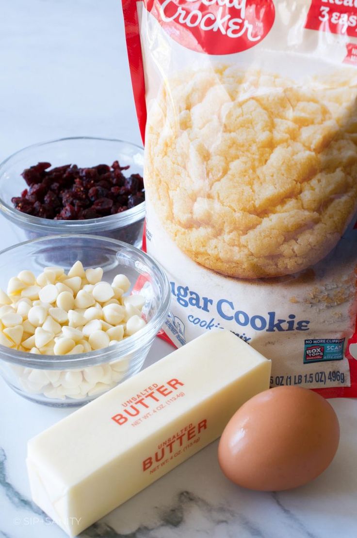 ingredients for cookies laid out on a marble counter top, including butter, eggs, cranberries, and sugar