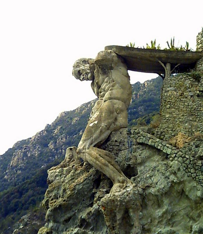 a statue on top of a rock near a mountain with trees in the back ground