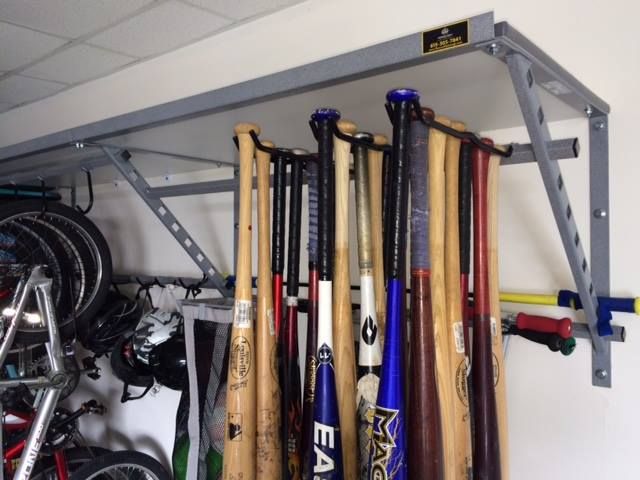 there are many baseball bats hanging on the wall in this garage storage area with bikes and other sports equipment