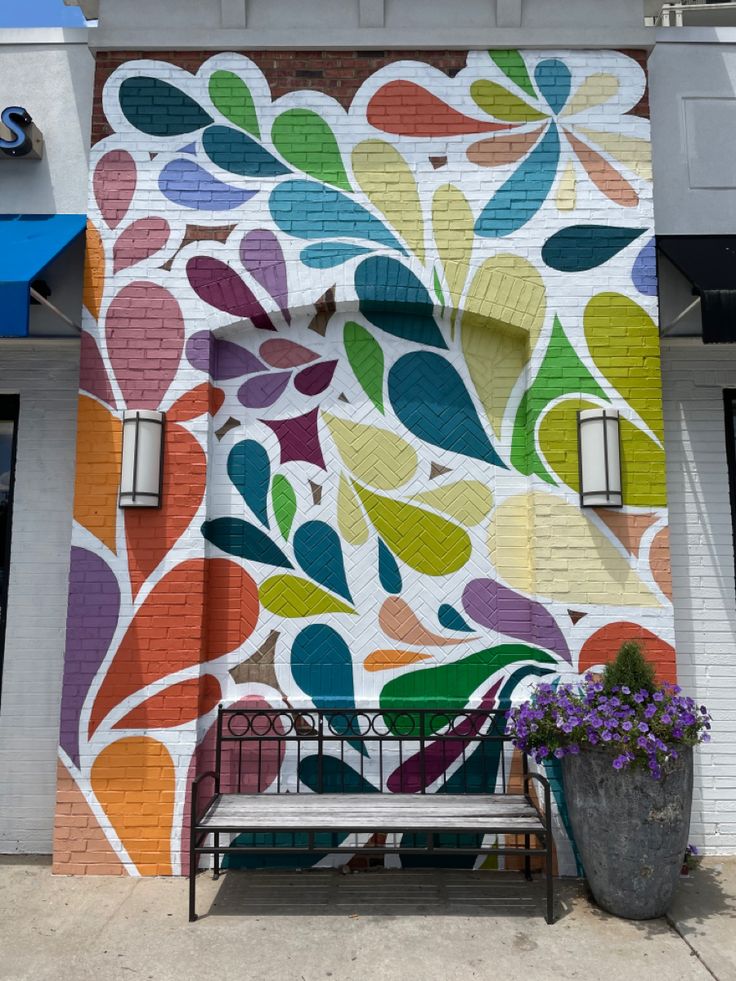 a colorful mural on the side of a building next to a planter with flowers in it